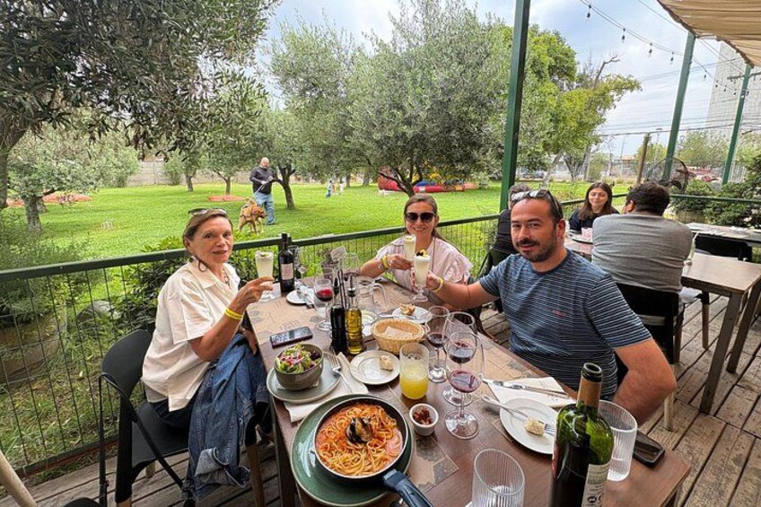 People dining outdoors at a table with food and drinks. 1