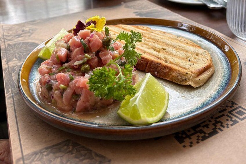 A plate of ceviche with lime wedges and a slice of bread on a ceramic plate. 2