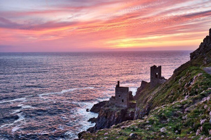 A coastal landscape with a sunset, rocky cliffs, and a ruined structure. 2