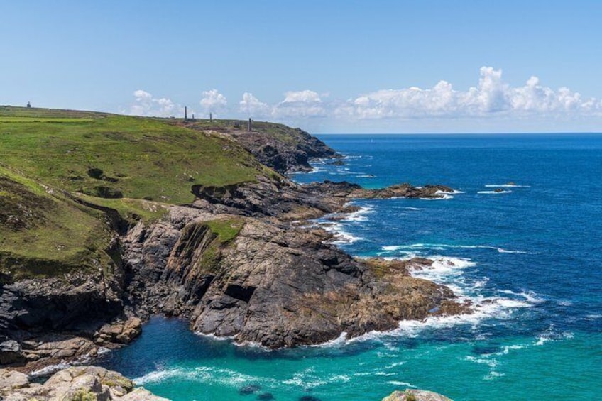 A coastal landscape with rocky cliffs, a grassy hill, and a clear blue sea. 3
