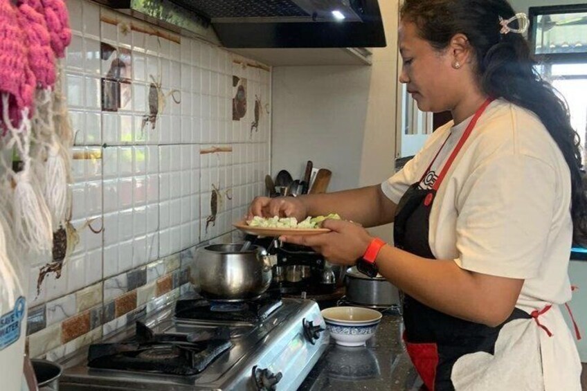 A person preparing food in a kitchen with tiled walls, a stove, and various cooking utensils. 3