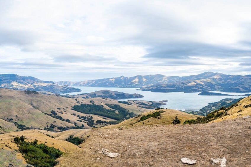 A panoramic view of a valley with rolling hills, a lake, and distant mountains under a cloudy sky. 2