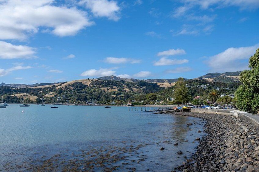 A coastal landscape with a rocky shoreline, calm water, boats, and distant hills. 3