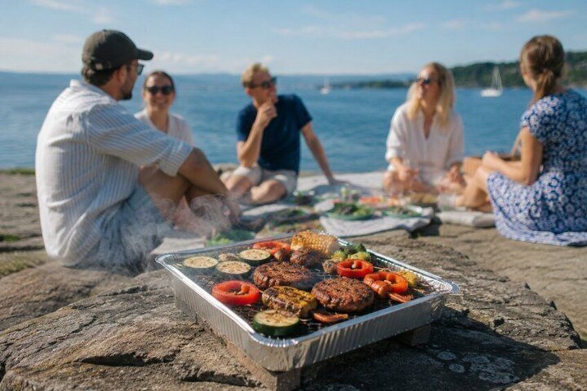 A group of people sitting on a rocky shore with a grill containing various meats and vegetables. 5