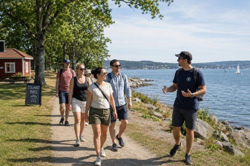 A group of people walking along a path by a lake with a sign for 'Island BBQ' visible. 3