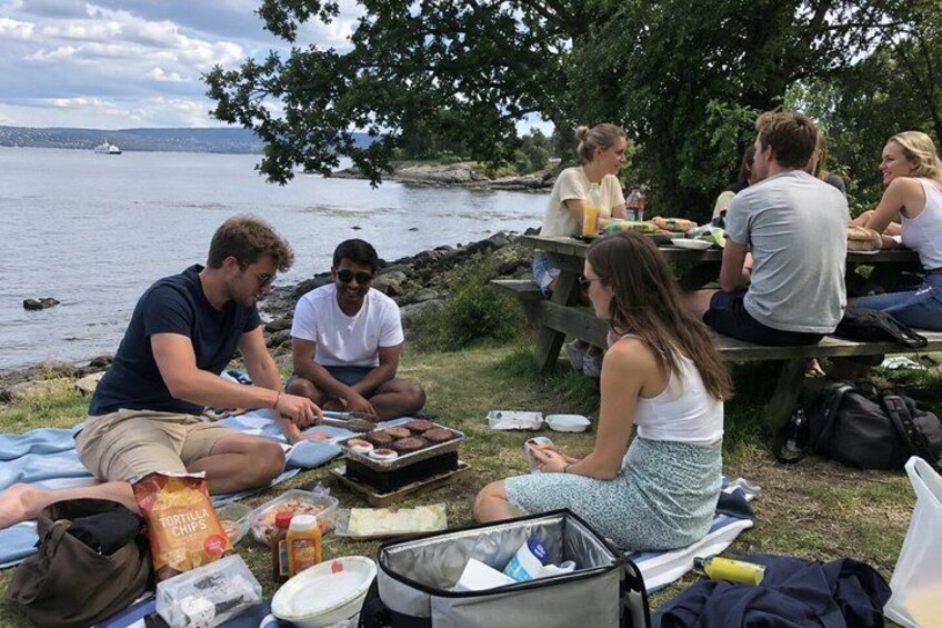 A group of people picnicking by a lakeside with food and drinks on a blanket. 4