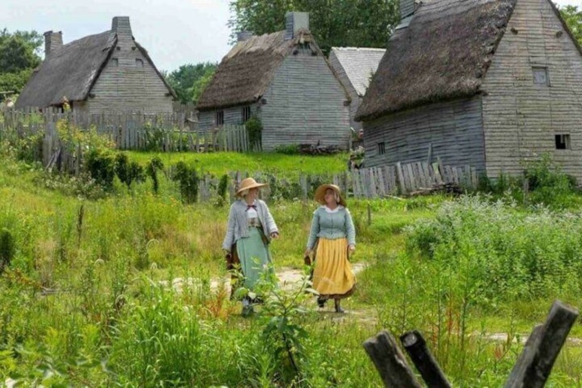 A rural village with thatched-roof cottages and two people walking through a grassy field. 1
