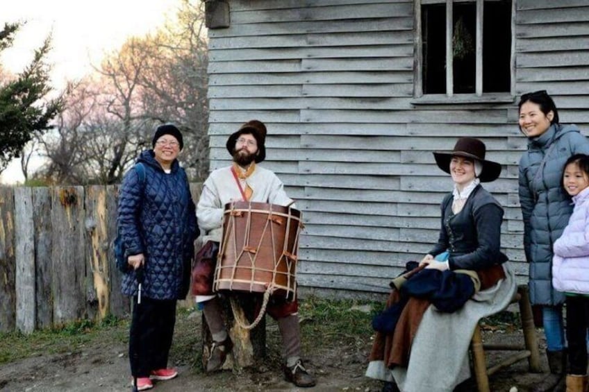 A group of people in historical costumes near a wooden house. 4