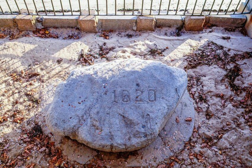 A large stone with the year 1820 engraved on it, surrounded by a sandy area with scattered leaves. 3