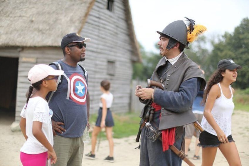 A historical reenactment scene with a man in a costume holding a sword, a woman in a white top, and a child in a pink hat. 3