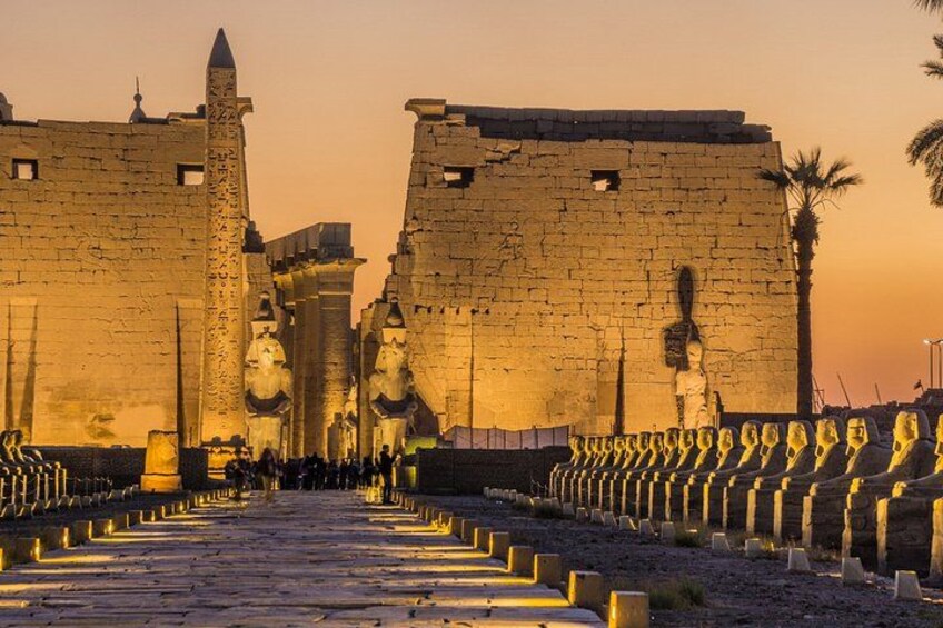 A historical site with ancient stone walls, a central obelisk, and rows of statues. 3