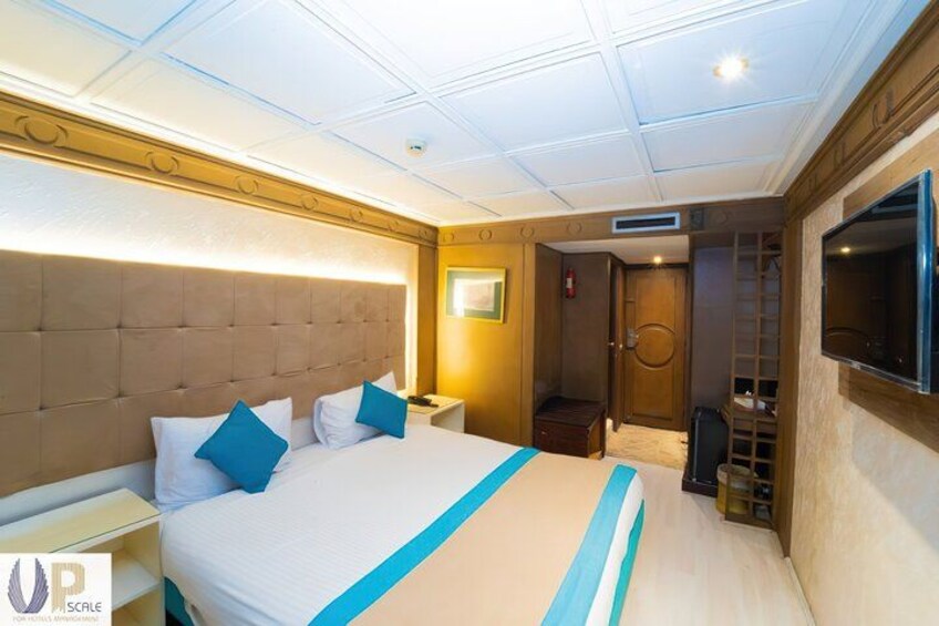 A hotel room with a large bed, a TV mounted on the wall, a bedside table, and a wardrobe. 2