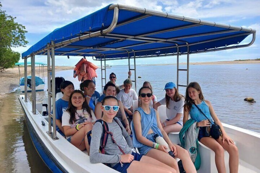 A group of people on a boat with a blue canopy, near a calm body of water and a sandy beach. 1