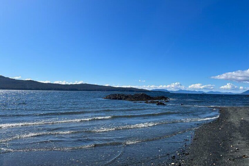 A beach with a rocky outcrop in the water, clear skies, and distant mountains. 5