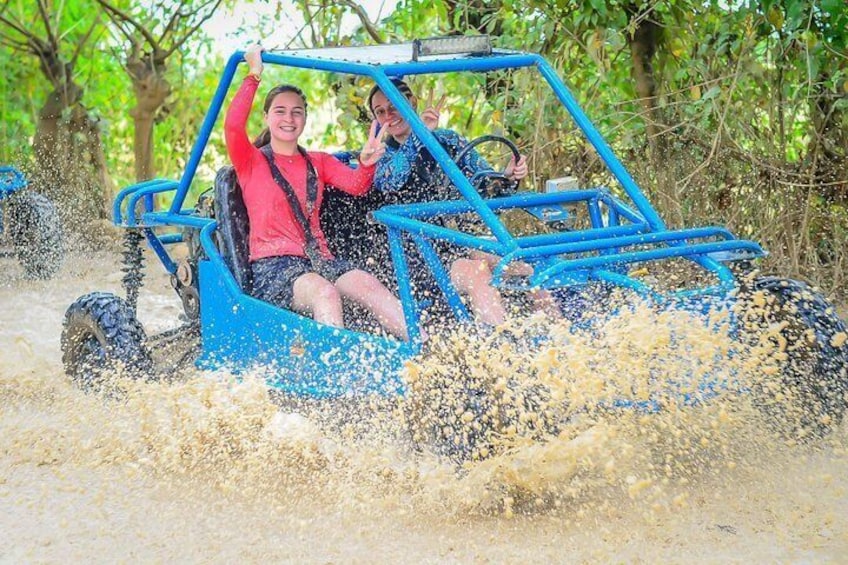 A blue off-road vehicle driving through a muddy area with water splashing around. 1