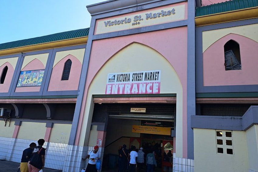 Victoria St. Market entrance with a sign, a tiled fence, and people entering. 1