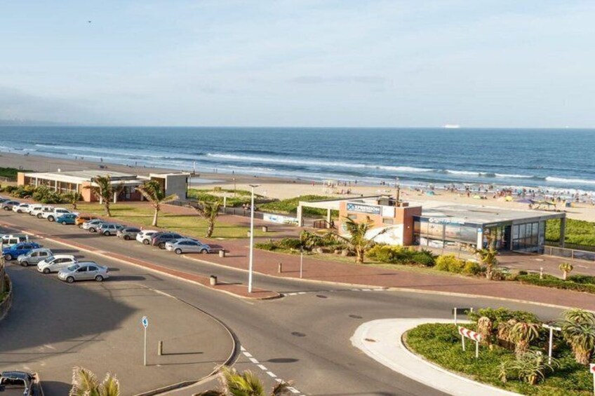 A coastal road with a beach, cars, and a building with a glass facade. 3