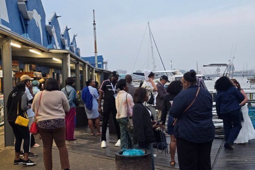 A group of people standing on a dock by the water, with boats in the background. 4