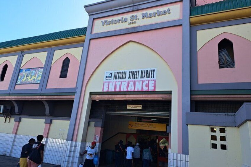 Victoria St. Market entrance with a sign, a tiled fence, and people entering. 1