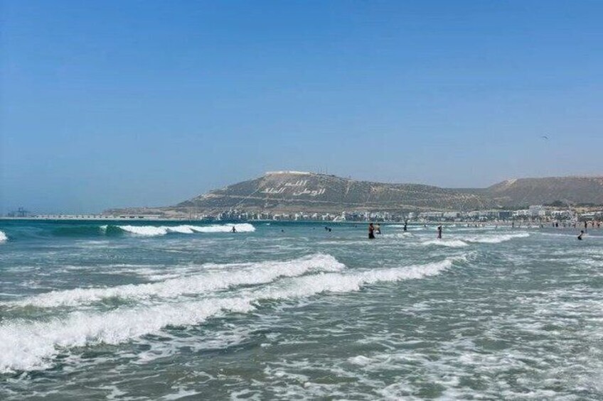 A beach with waves, people, and a mountain in the background. 5