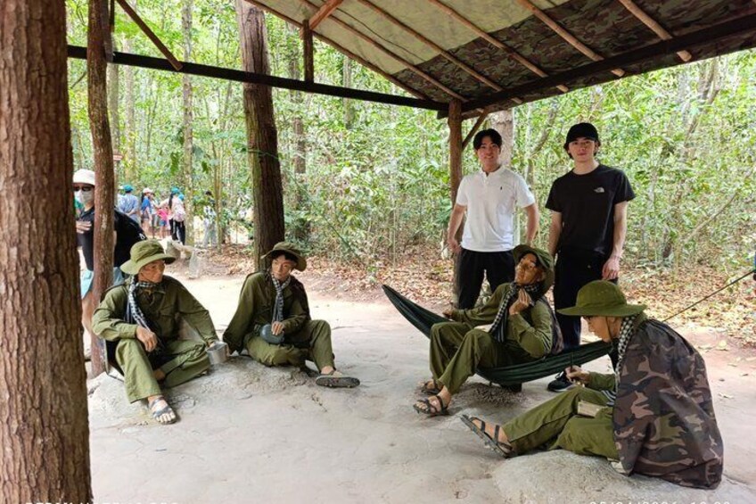People in outdoor gear sitting and standing under a shelter in a forest. 2