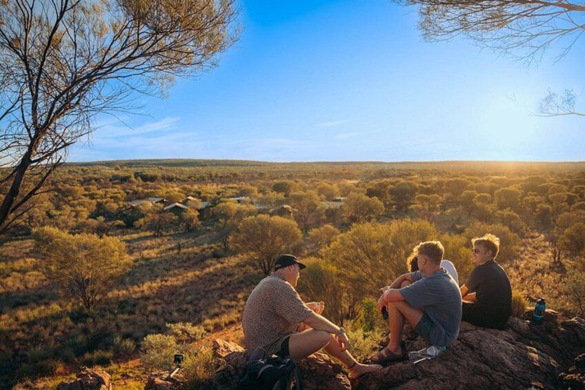 Three people sitting on a rock, overlooking a vast landscape with sparse vegetation and a clear sky. 2