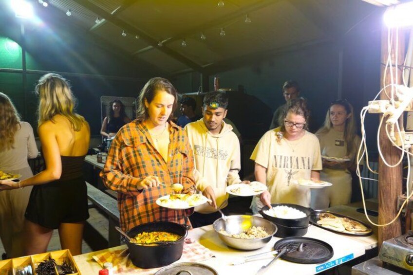 A group of people serving food at a buffet with various dishes and cooking equipment. 2
