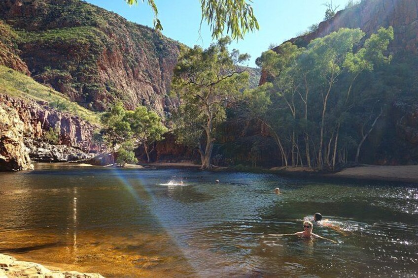 A river with swimmers, surrounded by cliffs and trees. 2