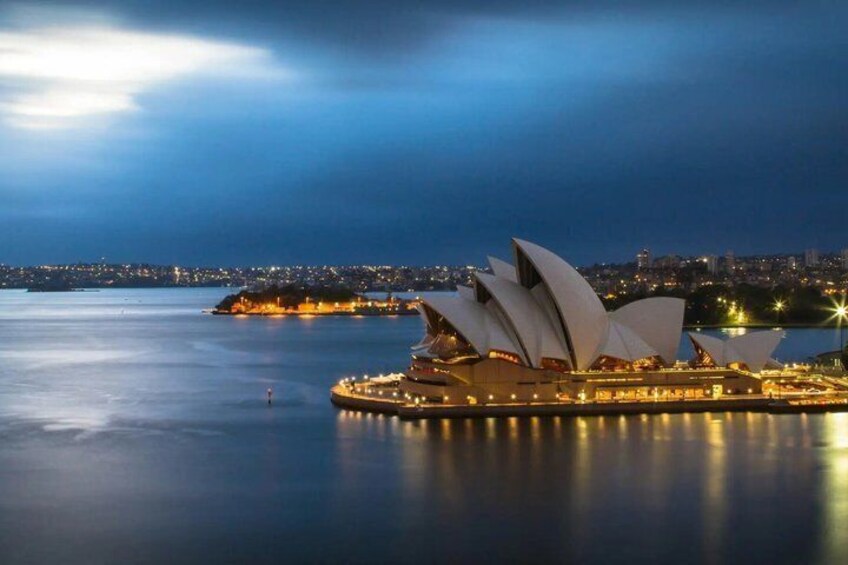 The Sydney Opera House with its distinctive sail-like design, surrounded by water and a cityscape in the background. 1