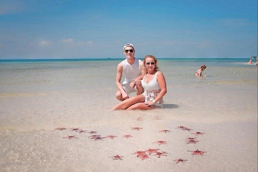 A couple sitting on a beach with a heart made of red objects in the sand. 2