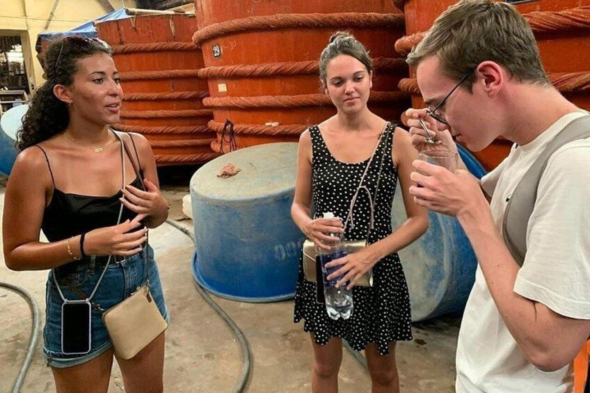 Three people standing in an industrial setting with large cylindrical tanks in the background. 3