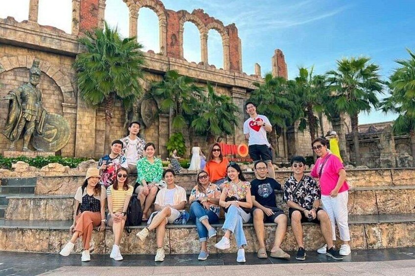 A group of people sitting on steps in front of a historical building with arches and statues. 4