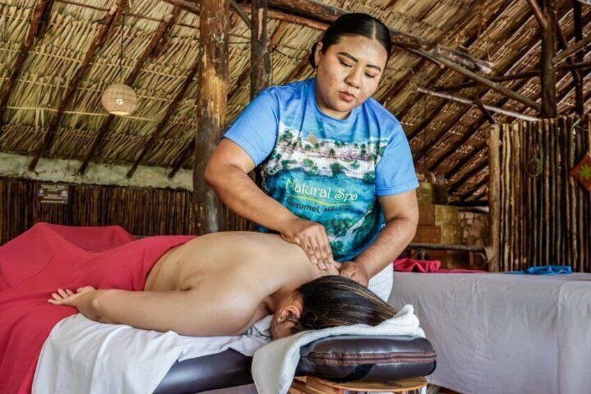 A person receiving a back massage in a rustic setting with a thatched roof. 1