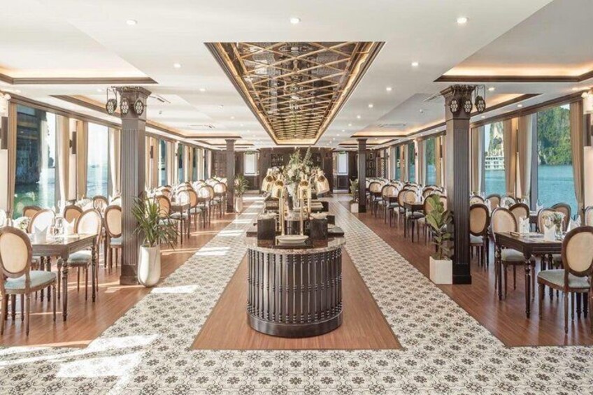 A spacious restaurant with a central bar, long tables, and large windows. 2