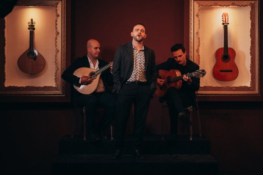 Three men on a stage with guitars, framed pictures of guitars on the walls. 3