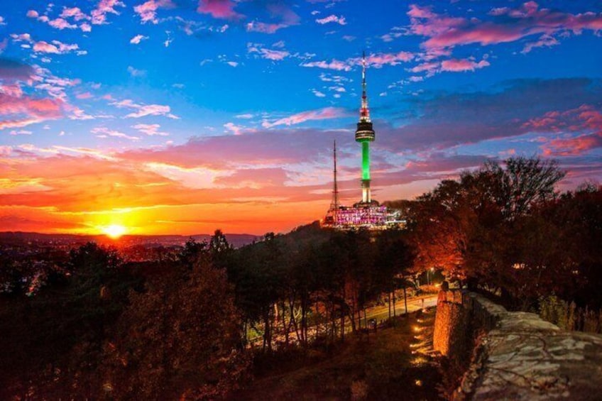 A tower with green lights, a sunset, and a forested landscape. 1