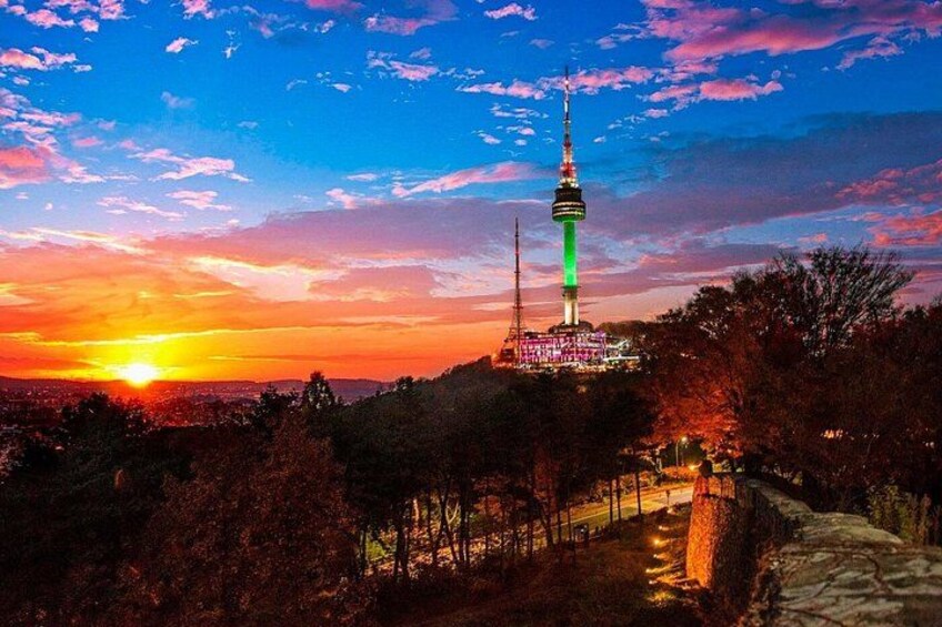 A tower with a spire, surrounded by trees and a sunset. 3