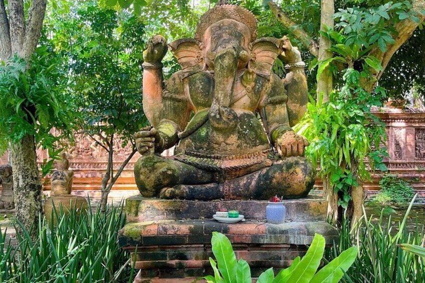 A large stone statue of a deity in a meditative pose, surrounded by lush greenery and traditional architecture. 2