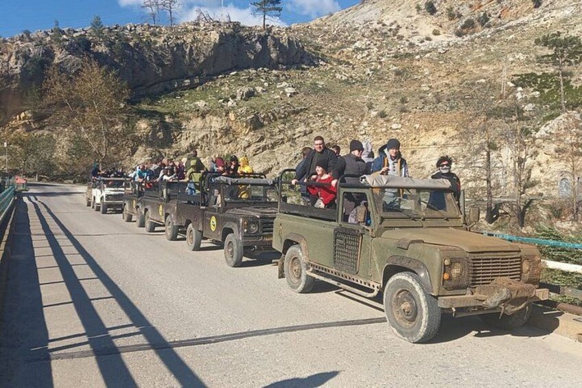 A convoy of jeeps on a road with passengers, surrounded by rocky terrain and sparse vegetation. 3