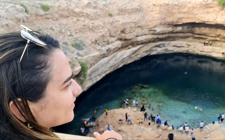 A person overlooking a natural rock formation with a clear water pool below. 5