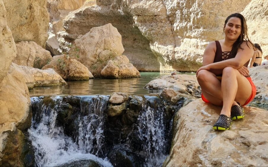 A person sitting on a rock by a waterfall in a rocky terrain. 3