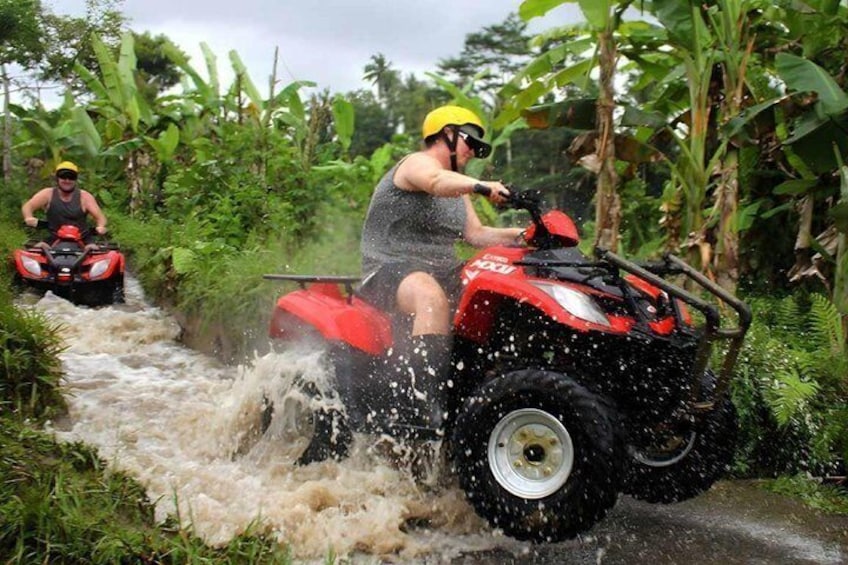 Two people on red all-terrain vehicles navigating a muddy water crossing. 3