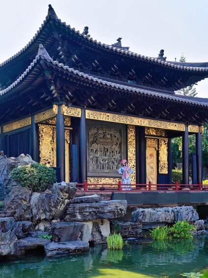 A traditional Chinese pavilion with ornate carvings and a pond with rocks and plants. 5