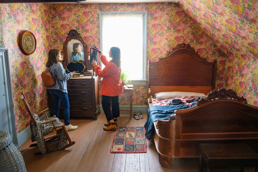A bedroom with floral wallpaper, a wooden bed, a rocking chair, and a dresser with a mirror. 5