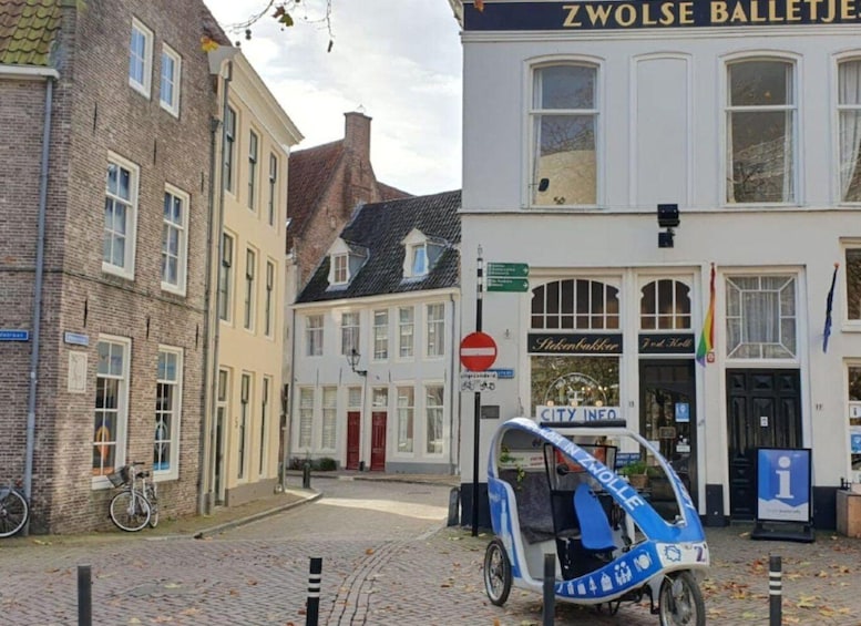 A cobblestone street with a blue electric vehicle parked in front of a building labeled 'ZWOLSE BALLETJE.' 1