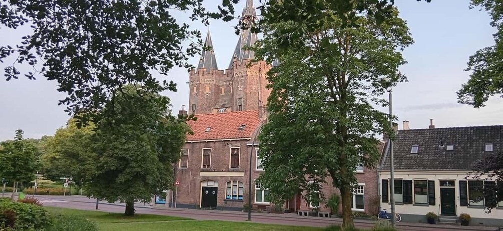 A historic building with a red brick facade and a tower, surrounded by trees and a paved street. 4