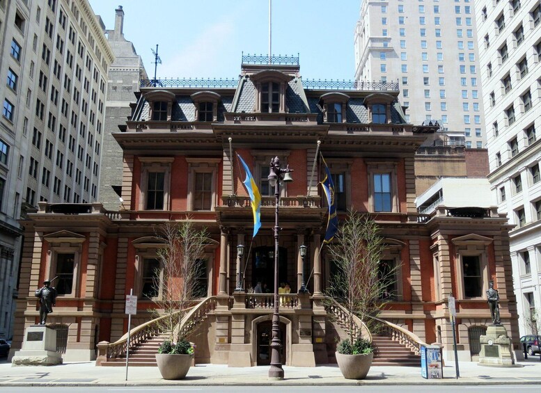 A historic building with a grand entrance, two large potted plants, and multiple flags. 2
