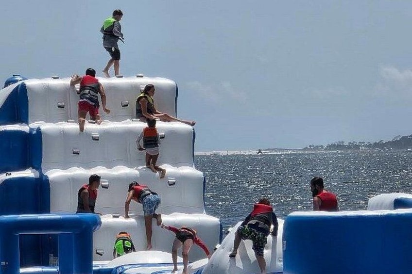 People climbing inflatable structures by a body of water. 3