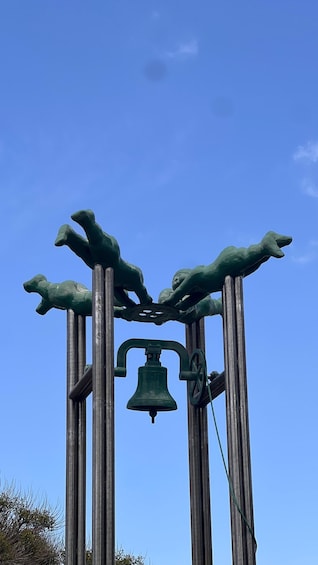 A green bell tower with a bell and a sculpture of hands reaching upwards. 4