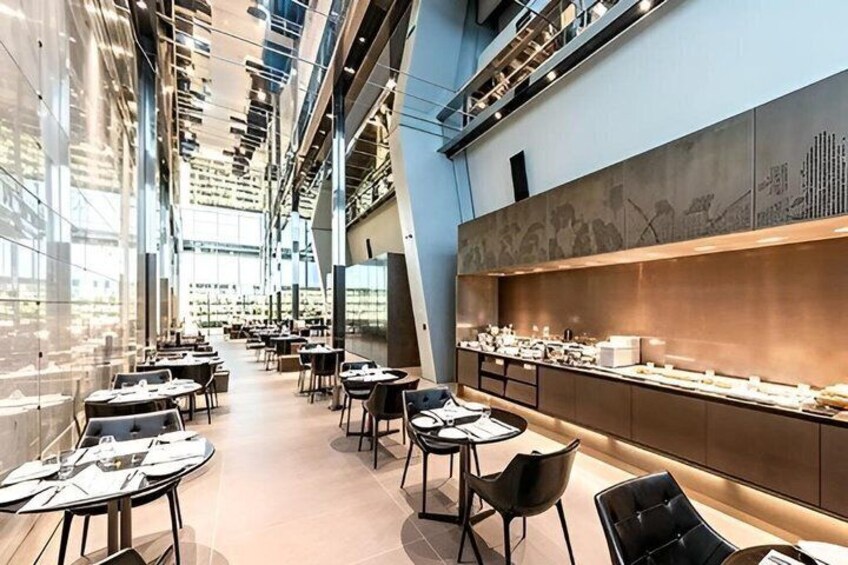 An indoor dining area with tables, chairs, and a long counter displaying food items. 3
